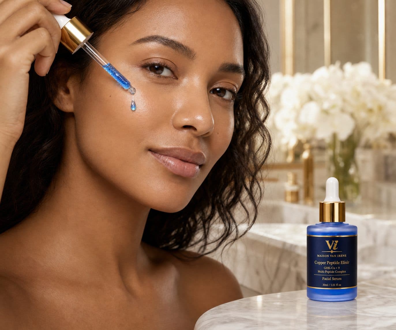 Woman applying Copper Peptide Elixir with the dropper — blue serum droplet on the cheek, bottle on a marble vanity