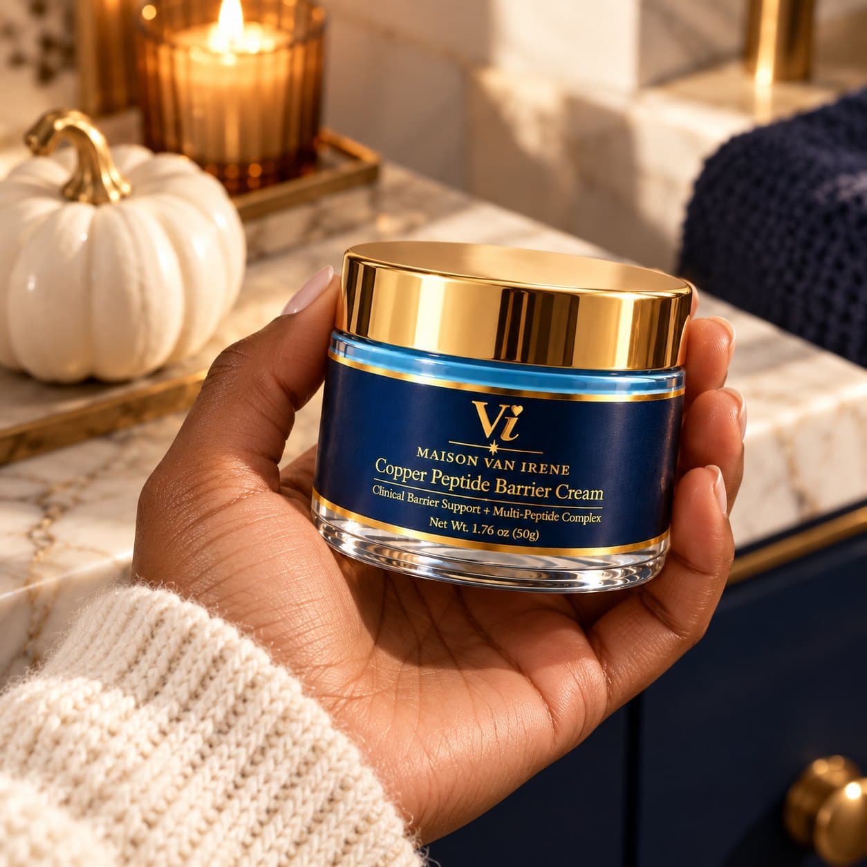 Copper Peptide Barrier Cream jar held in hand by candlelight, navy label and gold lid facing forward