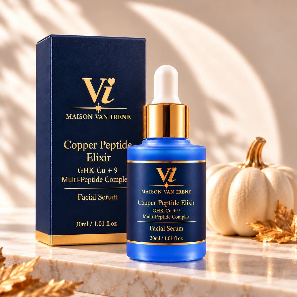 Maison Van Irene Copper Peptide Elixir royal-blue bottle and navy carton on a marble vanity with gold autumn leaves and white pumpkins