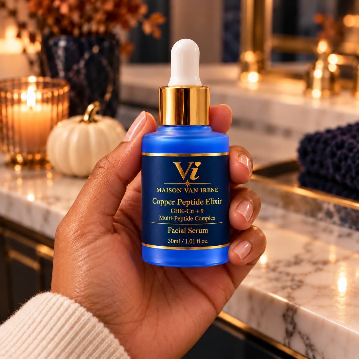 Copper Peptide Elixir 30ml bottle held in hand, label facing forward, with candles and small pumpkins behind