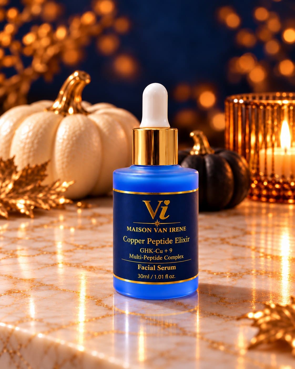 Maison Van Irene Copper Peptide Elixir royal-blue bottle with gold dropper collar on a marble counter, white and black pumpkins, gold leaves and candlelight behind — portrait crop for product cards